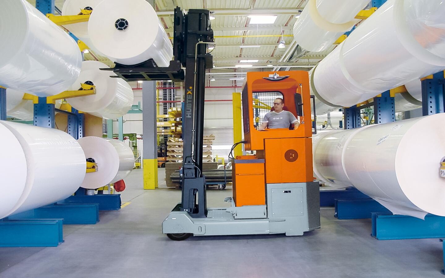 A reach truck handles rolls of paper